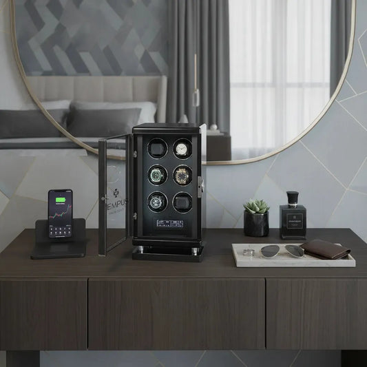 A modern wooden dresser holds a phone on a stand, the Tempus Luxury Watch Winder 6 with BioMetric Technology by Tempus for automatic watches, a small plant, cologne bottle, sunglasses, and wallet. A round mirror and bed are in the background.