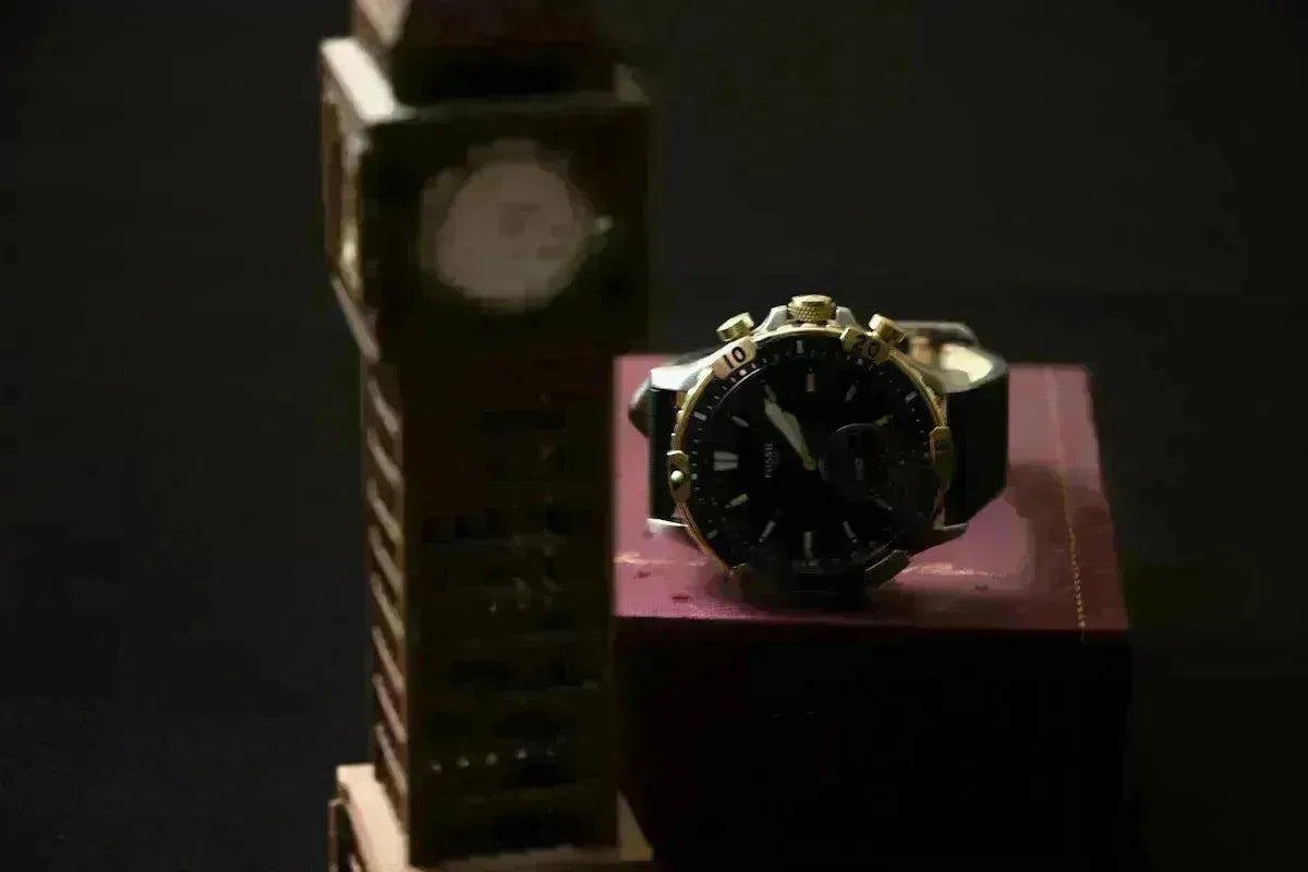 A black and gold watch resting on a burgundy Tempus box next to a miniature Big Ben clock tower model.