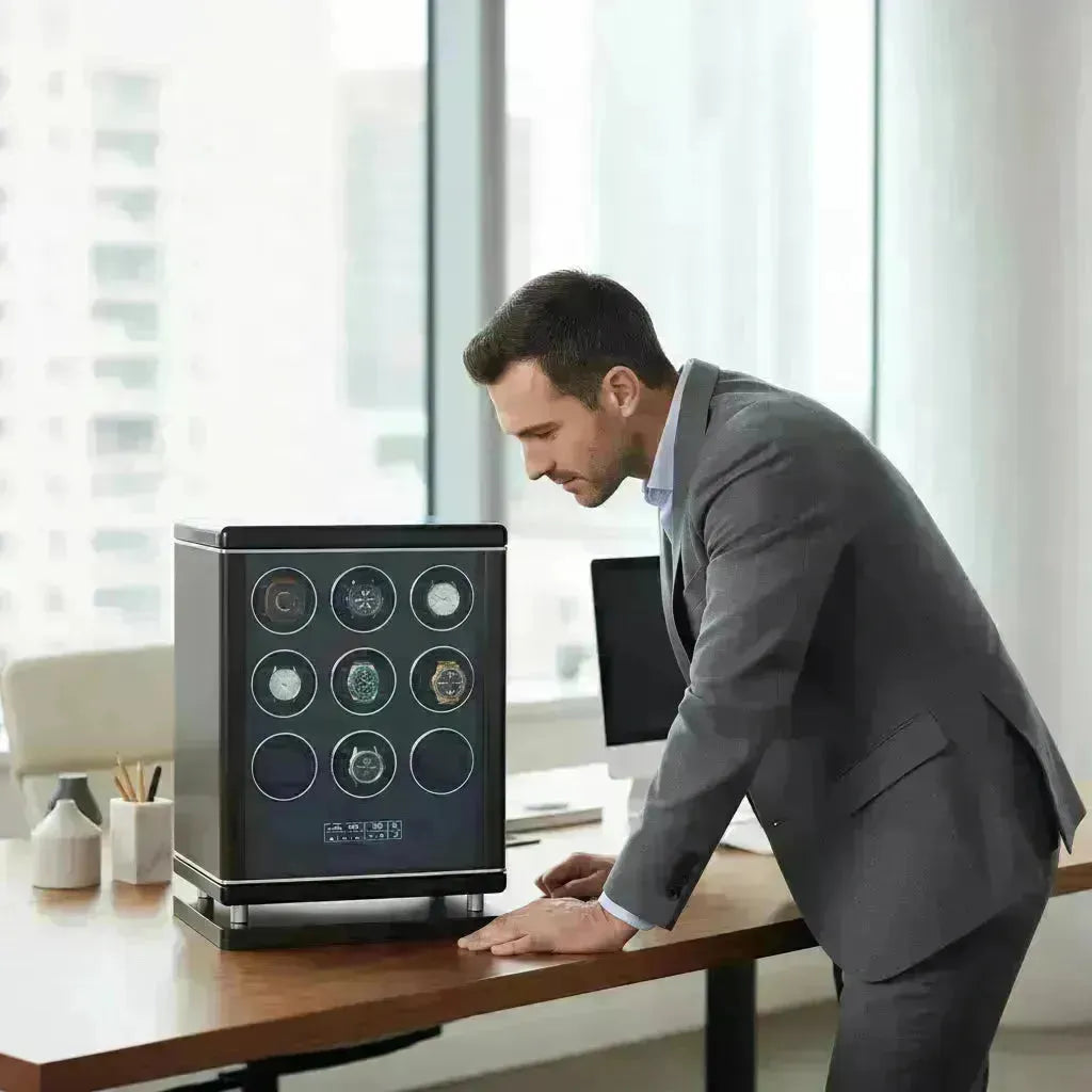 Man in a suit examining a sleek, black watch winder displaying nine automatic watches.