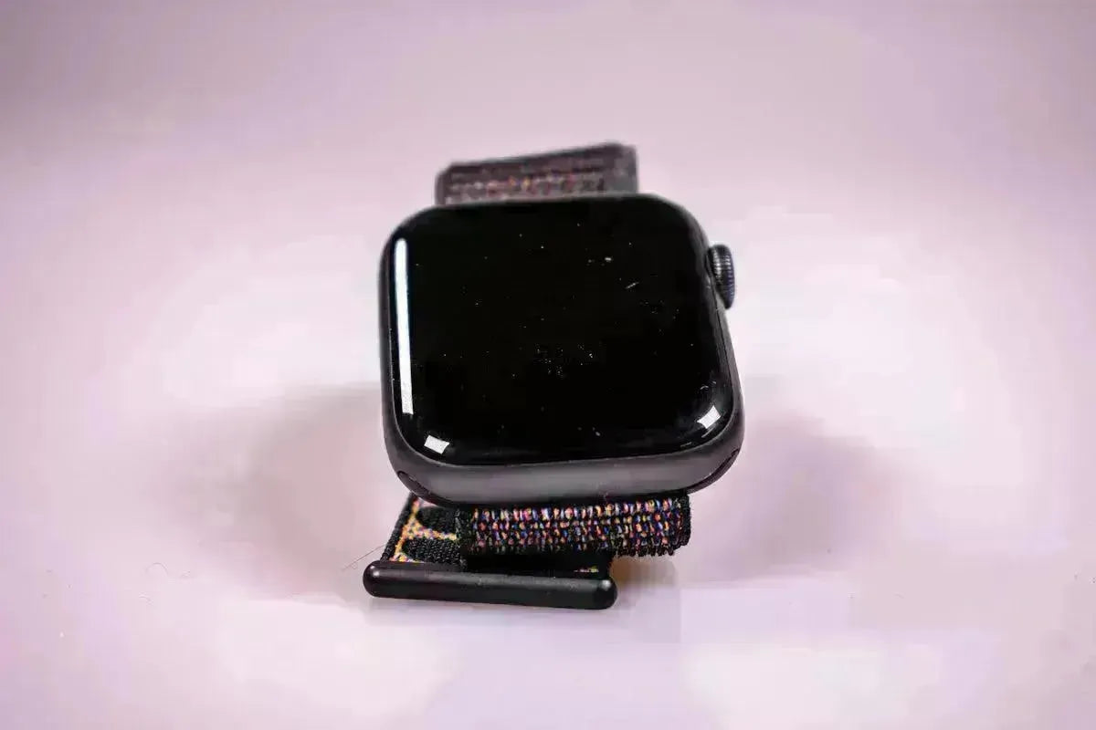 Black smartwatch with a textured, multicolored fabric strap resting on a smooth, light-colored surface.