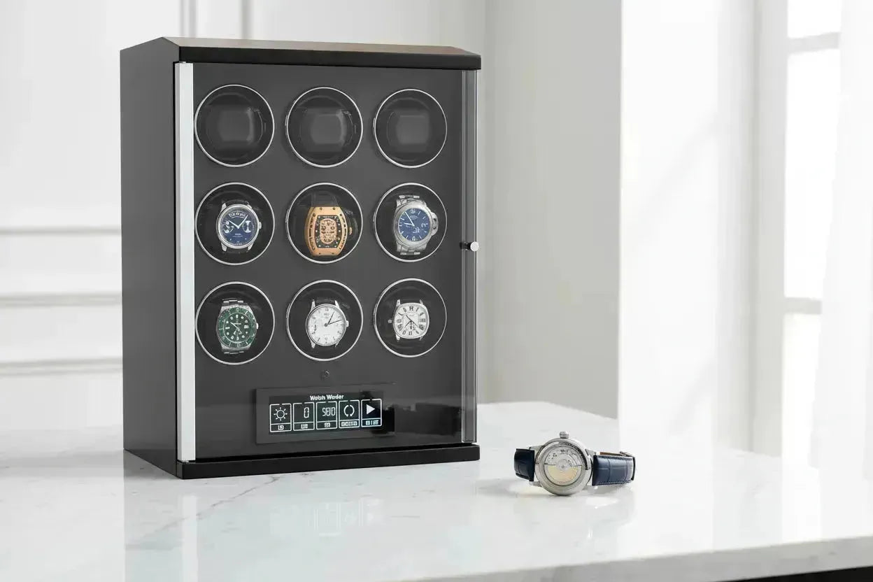 Black automatic watch winder displaying multiple luxury watches, with one watch on a marble surface.