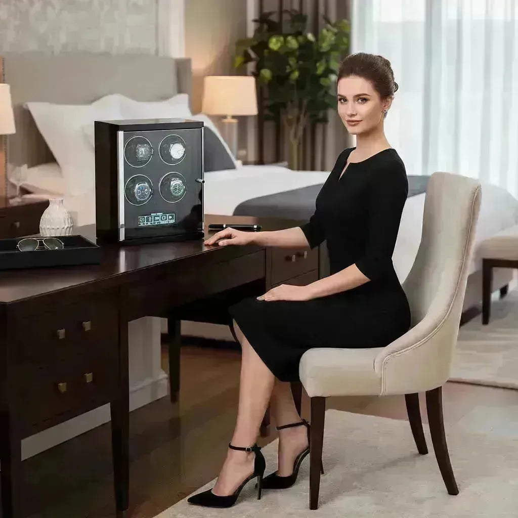 Elegant woman seated beside a black watch winder displaying four luxury watches in a bedroom setting.