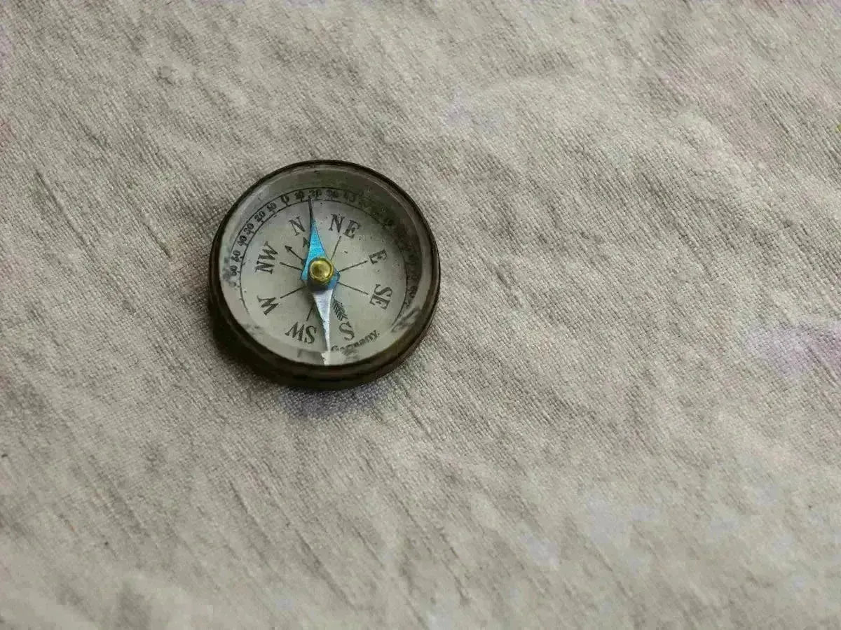 Vintage brass pocket compass with a blue needle resting on a textured grey fabric surface.
