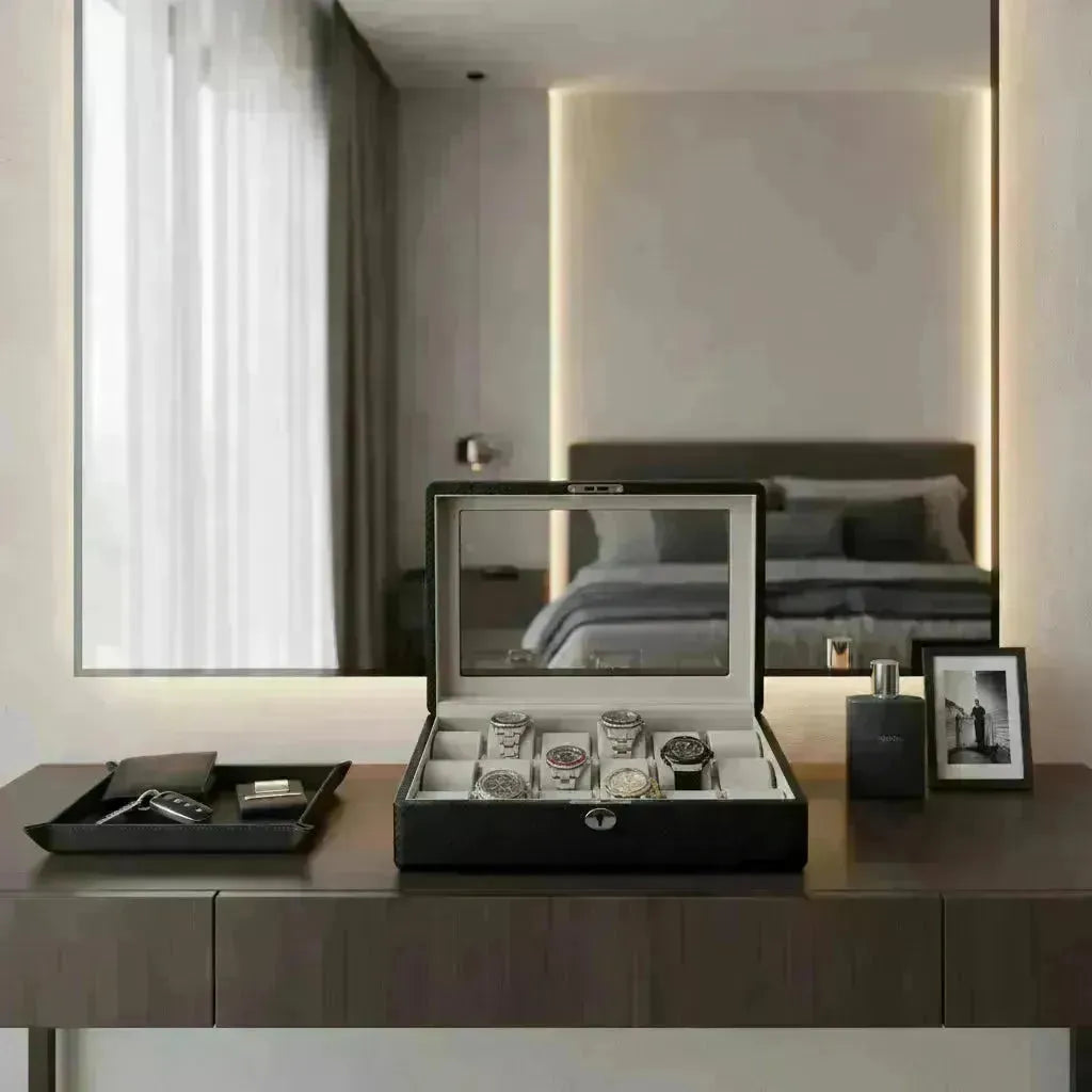 A black watch box with a clear lid displaying six automatic watches on a dresser.