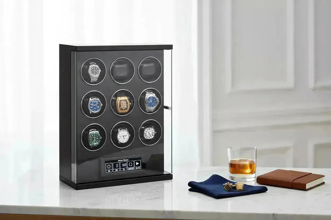 Black watch winder with nine luxury watches, a glass of whiskey, and cufflinks on a marble surface.