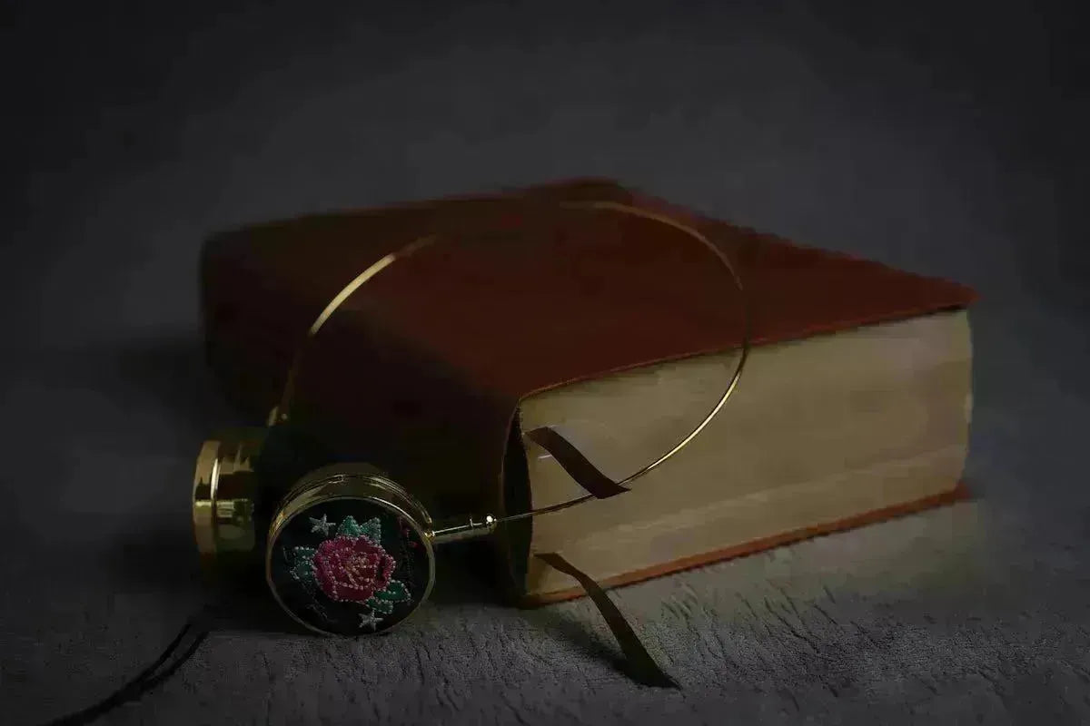 Vintage gold pocket watch with a floral rose design resting beside a rustic, leather-bound book on a dark surface.