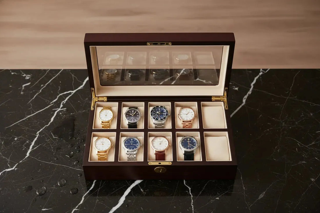 A dark wooden watch case with a glass top, displaying ten diverse wristwatches on a marble surface.