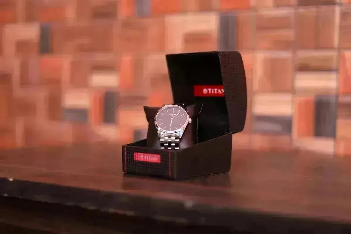 Titan watch with silver band and dark face in an open black box on a wooden surface.