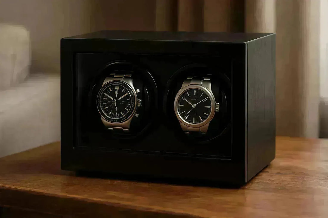 Two luxury watches displayed in a sleek, black wooden double watch winder on a polished table.