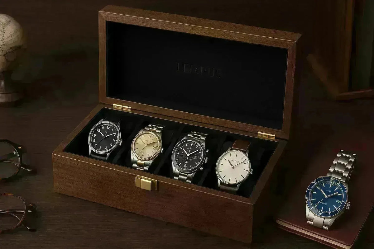 Elegant wooden Tempus watch box holding four luxury timepieces with a black velvet interior on a dark desk.
