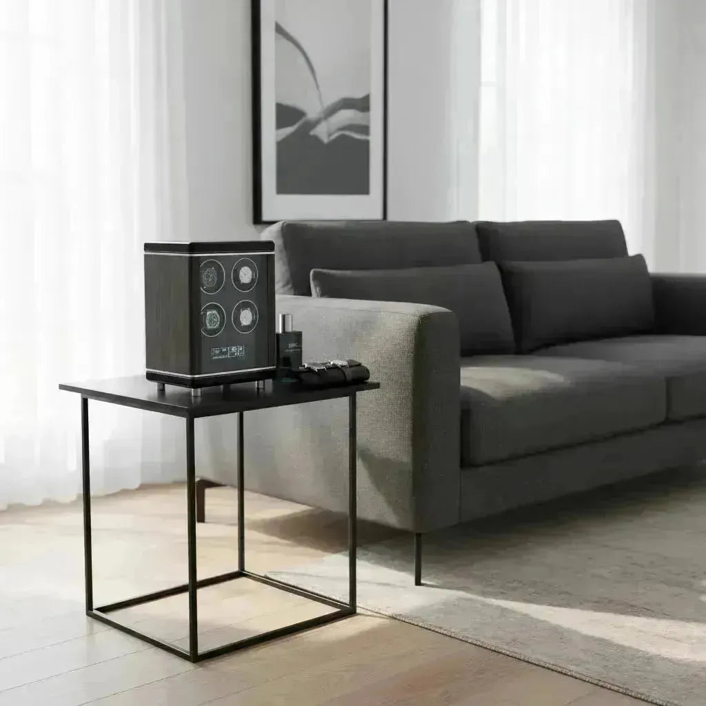 Modern dark wood watch winder with four display windows on a black side table in a minimalist living room.