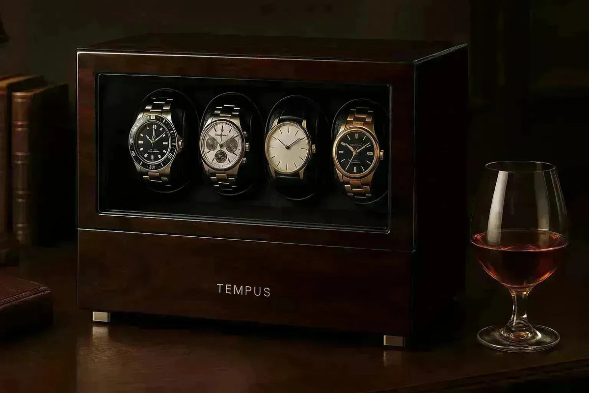 Dark wood Tempus watch winder holding four luxury timepieces next to a glass of cognac on a desk.