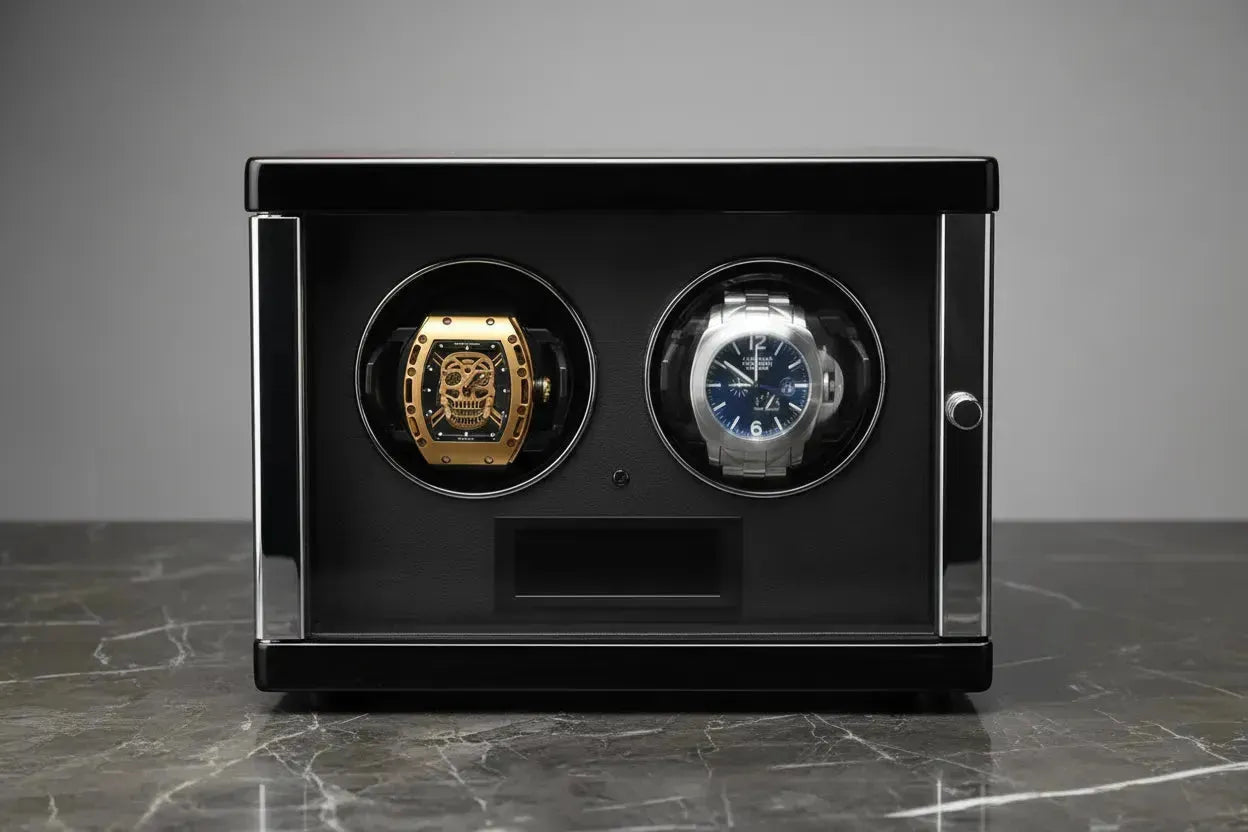 Black dual watch winder holding a gold skull-dial watch and a silver watch with a blue face on a marble surface.