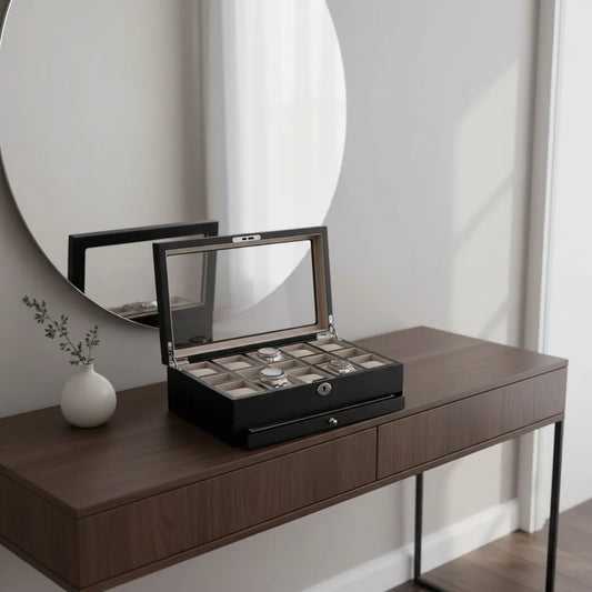 A Tempus Luxury Watch Winders 10 Watch Box in black oak veneer with an extra storage drawer sits on the console, displaying several watches. Next to it, a small white vase with green sprigs rests below a round mirror on the light wall.
