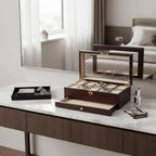 The Tempus Luxury Watch Winders 10 Watch Box, with a premium cherry wood satin finish and extra storage drawer, sits open on a marble vanity displaying watches; nearby are glasses, a black tray, bottle, and folded cleaning cloth.