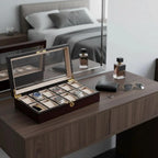 A Tempus Luxury Watch Winders 12 Watch Box in Premium Cherry Wood Satin Finish sits open on a brown dresser, surrounded by sunglasses, a black wallet, a perfume bottle, and the bed's reflection in the mirror above.