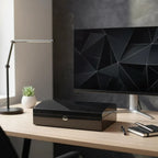 Black carbon fibre 12-watch box with a curved lid and silver lock, displayed on a modern desk.