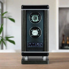 The Tempus Luxury Watch Winders 2 Watch Winder for Automatic Watches For Men with BioMetric Access Technology features a black and silver design, digital controls, and holds two watches, displayed on a wooden surface with plants and shelves in the blurred background.