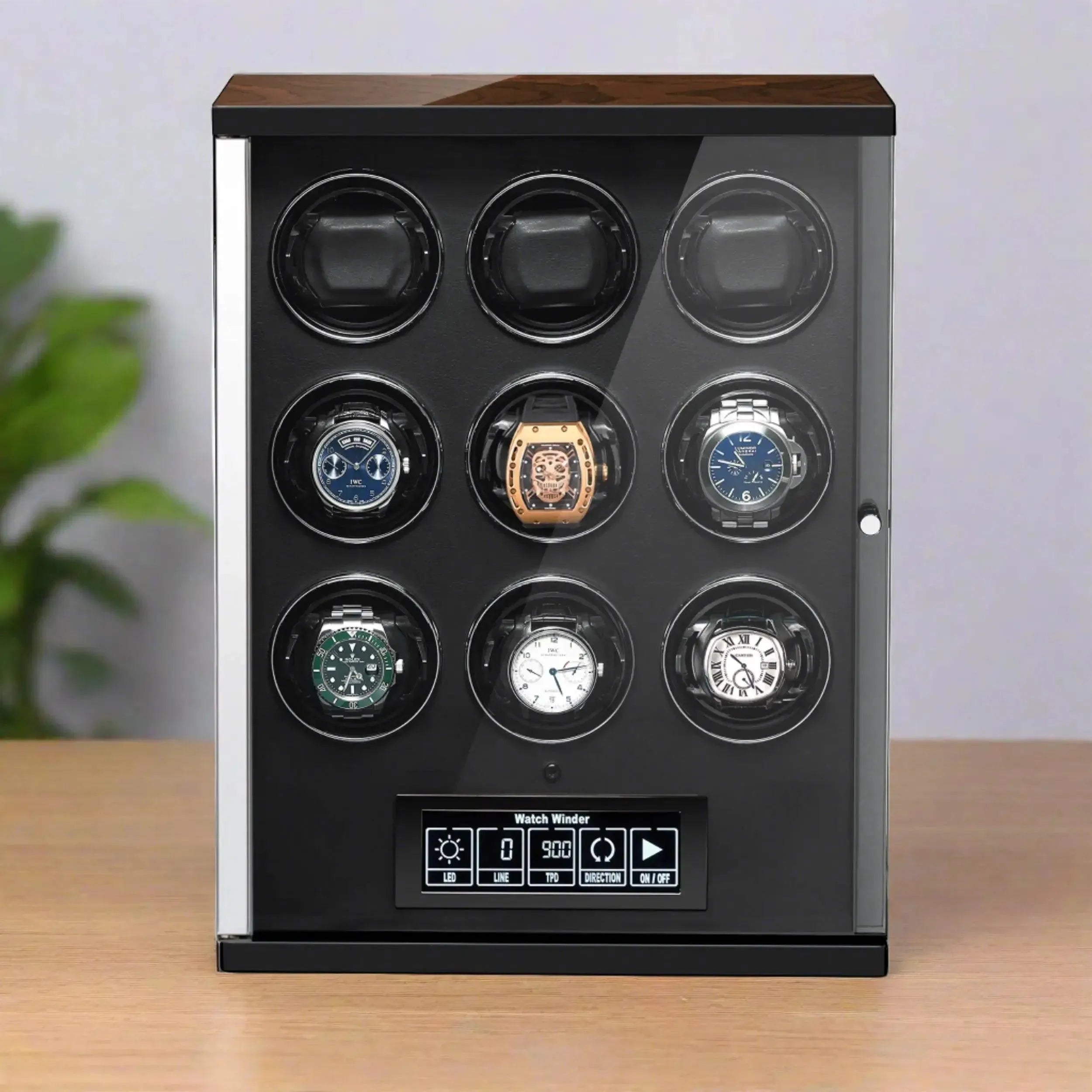 The Tempus Luxury Watch Winders 9 Watch Winder for Automatic Watches features individual rotating slots, a glass front, and touch screen technology. It sits on a wooden surface with a green plant in the background.