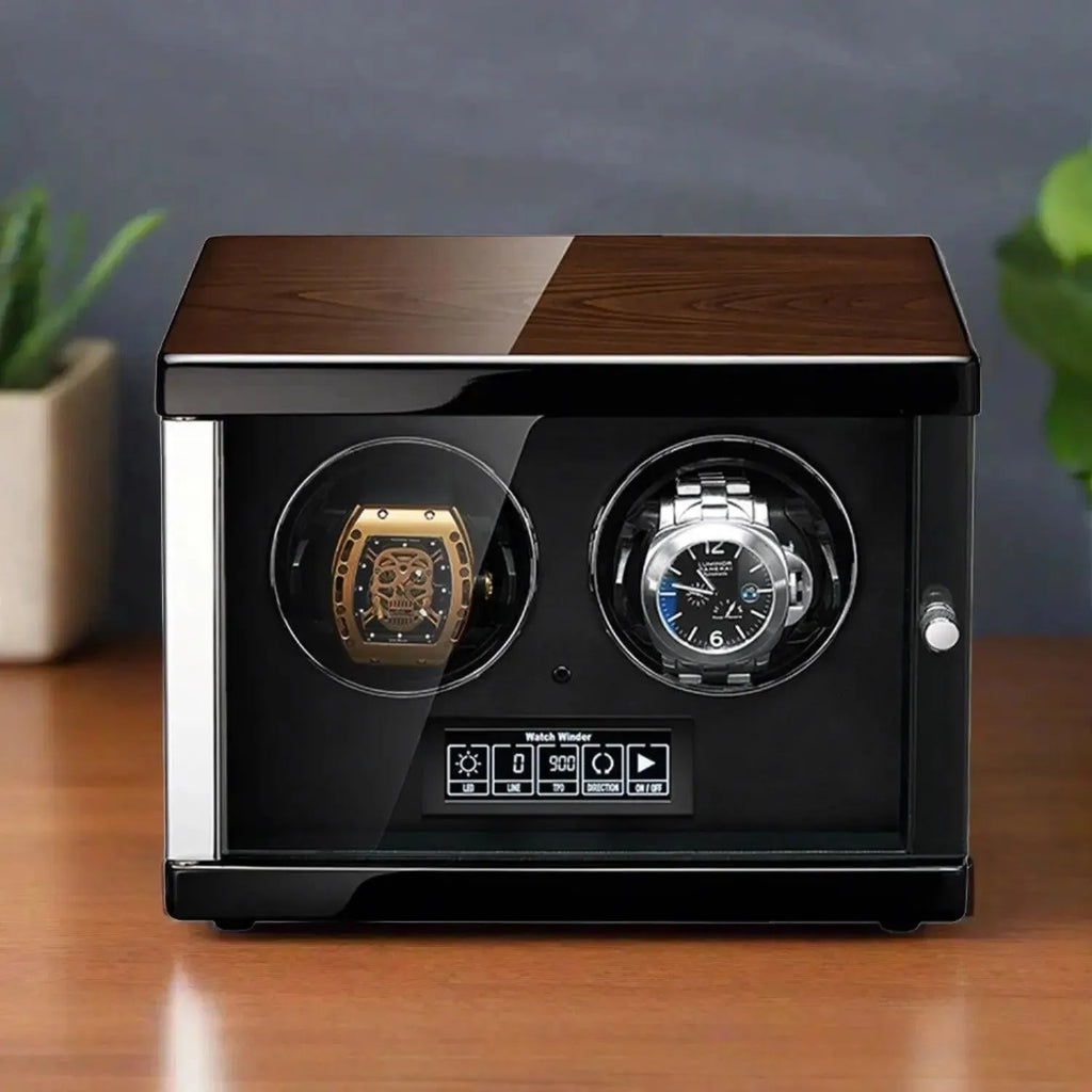 The Tempus 2 Watch Winder Automatic by Tempus Luxury Watch Winders features a wooden top, black sides, and a glass front displaying two luxury watches; it rests on a wooden surface with a blurred plant in the background.