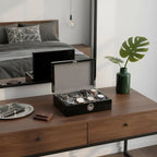 A dresser showcases the Tempus 8 Watch Box in Black Piano Finish with Bio Metric Lock by Tempus Luxury Watch Winders storing eight watches, alongside a green vase with monstera leaf, sunglasses on a tray, and a wallet. The mirror reflects the bed and decor.