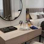 A modern bedroom showcases the Tempus Double White Marble Watch Stand Dark Violet Veins with Black Leather by Tempus Luxury Watch Winders, holding two watches, sunglasses, a wallet, polka dot handkerchiefs, and a round mirror; bed and drink in background.