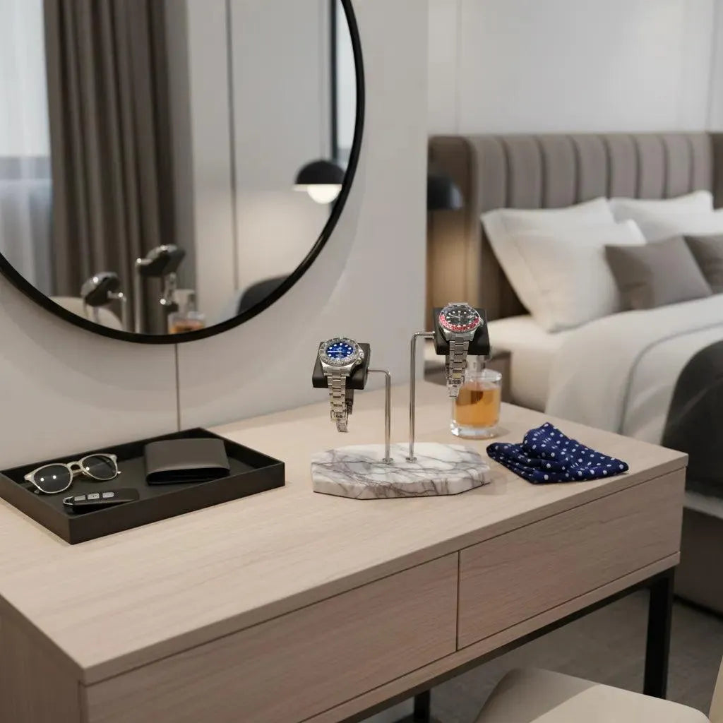 A modern bedroom showcases the Tempus Double White Marble Watch Stand Dark Violet Veins with Black Leather by Tempus Luxury Watch Winders, holding two watches, sunglasses, a wallet, polka dot handkerchiefs, and a round mirror; bed and drink in background.