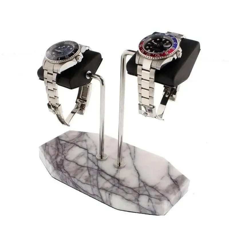 Two stainless steel watches rest on black leather cushions atop the Tempus Double White Marble Watch Stand with dark violet veins by Tempus Luxury Watch Winders, elegantly supported on a white marble base.