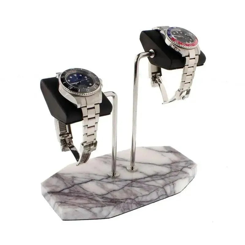 Two silver wristwatches rest on the Tempus Double White Marble Watch Stand (Dark Violet Veins, Black Leather) by Tempus Luxury Watch Winders, featuring a marble-patterned base and metal arms on a plain white background.