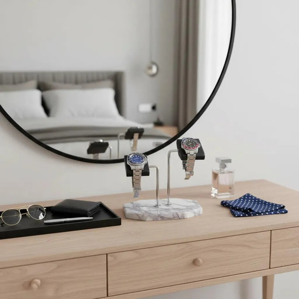 A wooden dresser displays sunglasses, a wallet, cologne, polka-dot handkerchiefs, and two wristwatches on the Tempus Double White Marble Watch Stand Dark Violet Veins with Black Leather by Tempus Luxury Watch Winders. A round mirror reflects a bed and curtains.