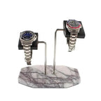 Two silver wristwatches are displayed on the Tempus Double White Marble Watch Stand Dark Violet Veins with Black Leather by Tempus Luxury Watch Winders, featuring a blue-faced watch on the left and a black face with red and blue bezel on the right.