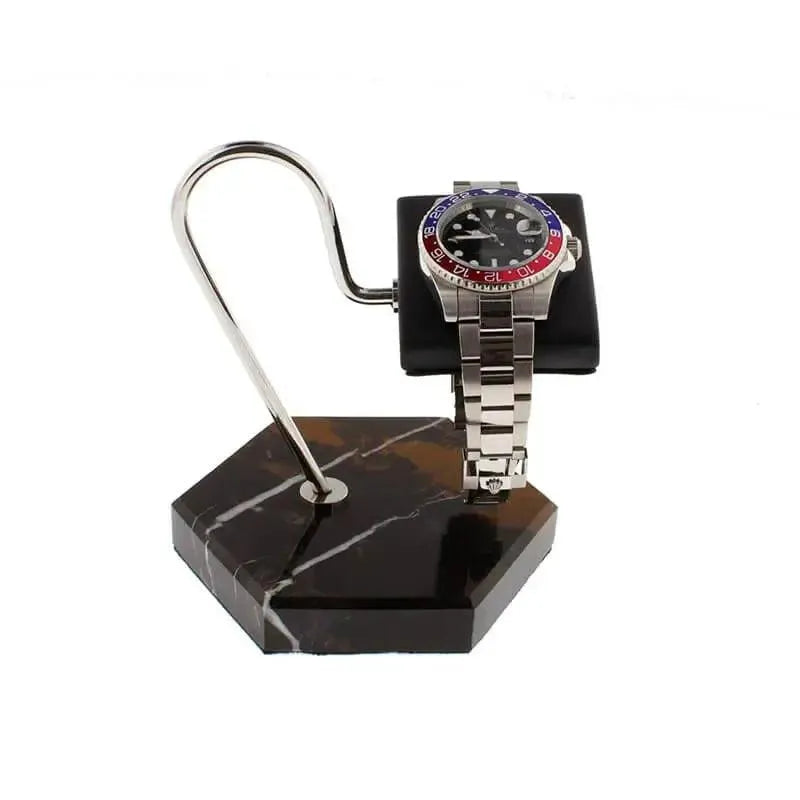 A silver wristwatch with a blue and red bezel rests on a black cushion, displayed atop the Tempus Watch Stand in Black Marble Brown Veining with Black Leather by Tempus Luxury Watch Winders against a crisp white background.