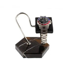 A silver wristwatch with a blue and red bezel rests on a black cushion, displayed atop the Tempus Watch Stand in Black Marble Brown Veining with Black Leather by Tempus Luxury Watch Winders against a crisp white background.