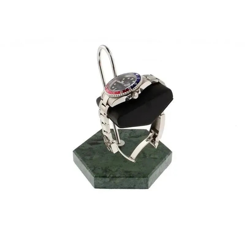 A silver wristwatch with a red and blue bezel rests on a black cushion atop the Tempus Watch Stand in Green Marble Hexagon Base with Black Leather by Tempus Luxury Watch Winders, set against a white background.