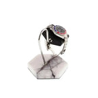 A silver wristwatch is displayed on the Tempus White Marble Watch Stand Dark Violet Veins with Black Leather by Tempus Luxury Watch Winders, featuring a hexagonal design and curved metal holder against a white background.