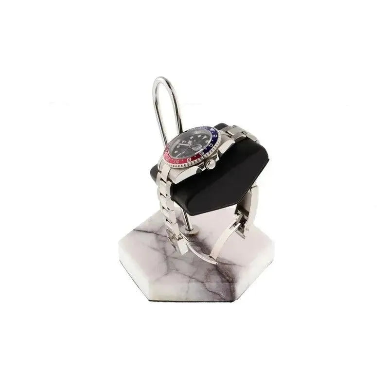 A silver wristwatch with a red and blue bezel sits on a black cushion atop the Tempus White Marble Watch Stand Dark Violet Veins with Black Leather by Tempus Luxury Watch Winders, displayed against an elegant white background.