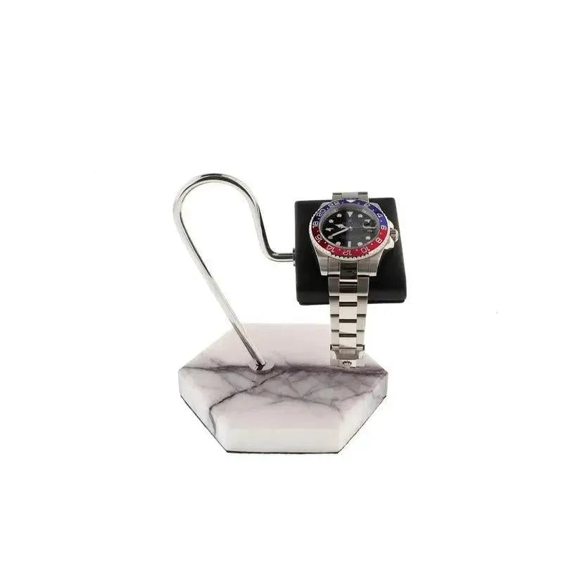 A silver wristwatch with a two-tone blue and red bezel is displayed on the Tempus White Marble Watch Stand Dark Violet Veins with Black Leather by Tempus Luxury Watch Winders, featuring a hexagonal base and curved metal holder.
