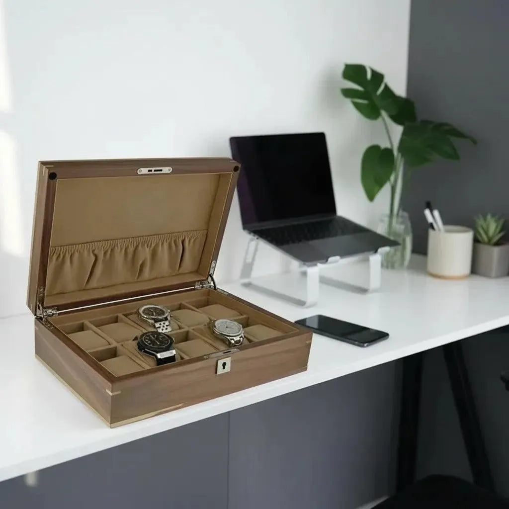 Open light walnut wood watch box with a glass lid, plush suedette interior, holding three watches on a white desk.