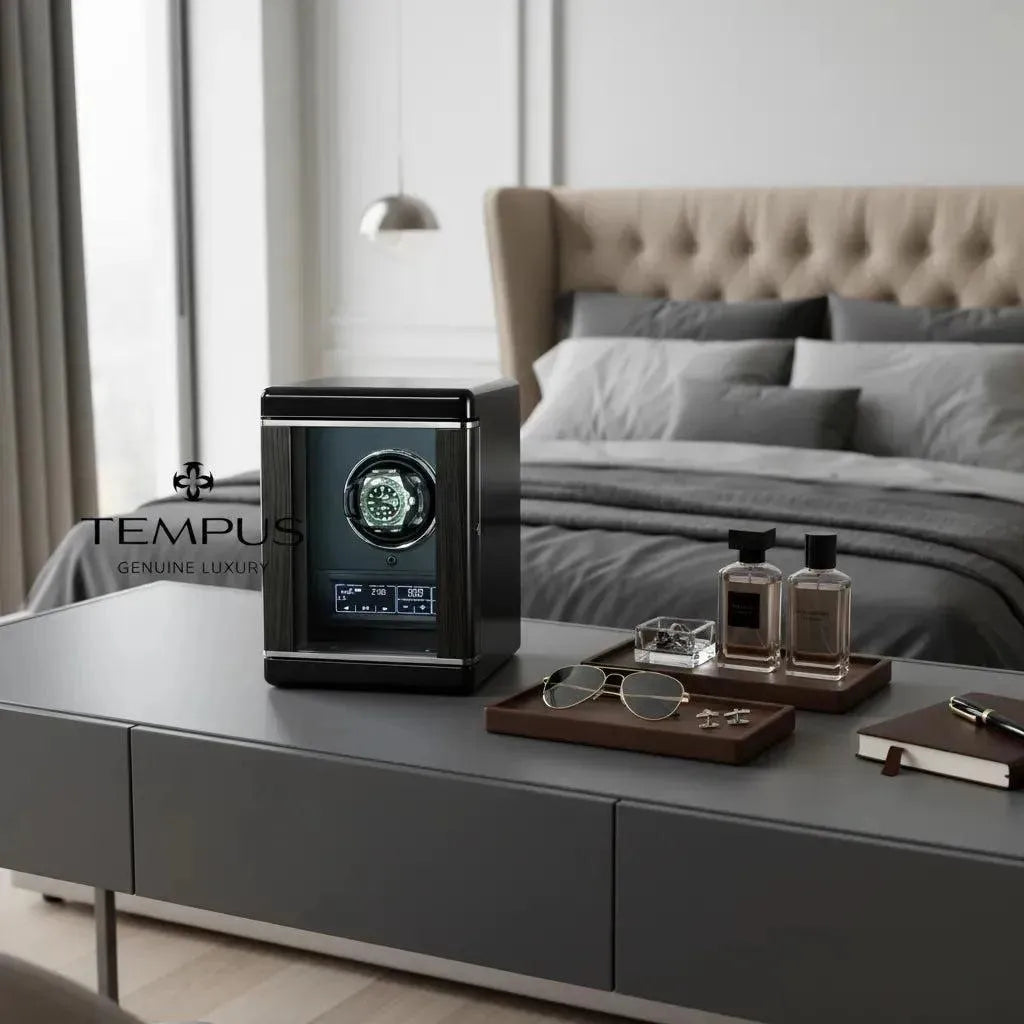 A modern bedroom with a neatly made bed and gray bedding features a gray table displaying perfumes, sunglasses, cufflinks, and the Tempus Luxury Watch Winders’ Watch Winder for 1 Automatic Watch with Remote Control. The Tempus logo appears on the left.