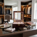 Close-up of cherry wood watch box with refined interior and watches, in an elegant dressing room with luxury props and warm lighting.
