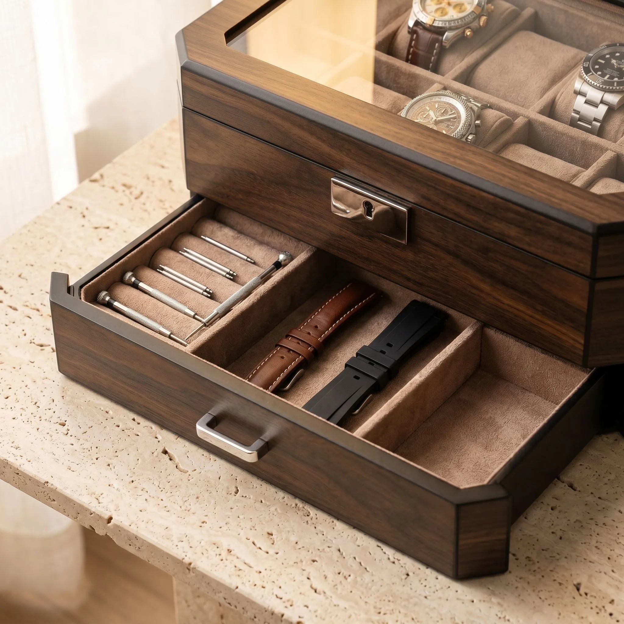 Close-up of open watch box lower drawer with neatly arranged straps and accessories on textured stone surface.