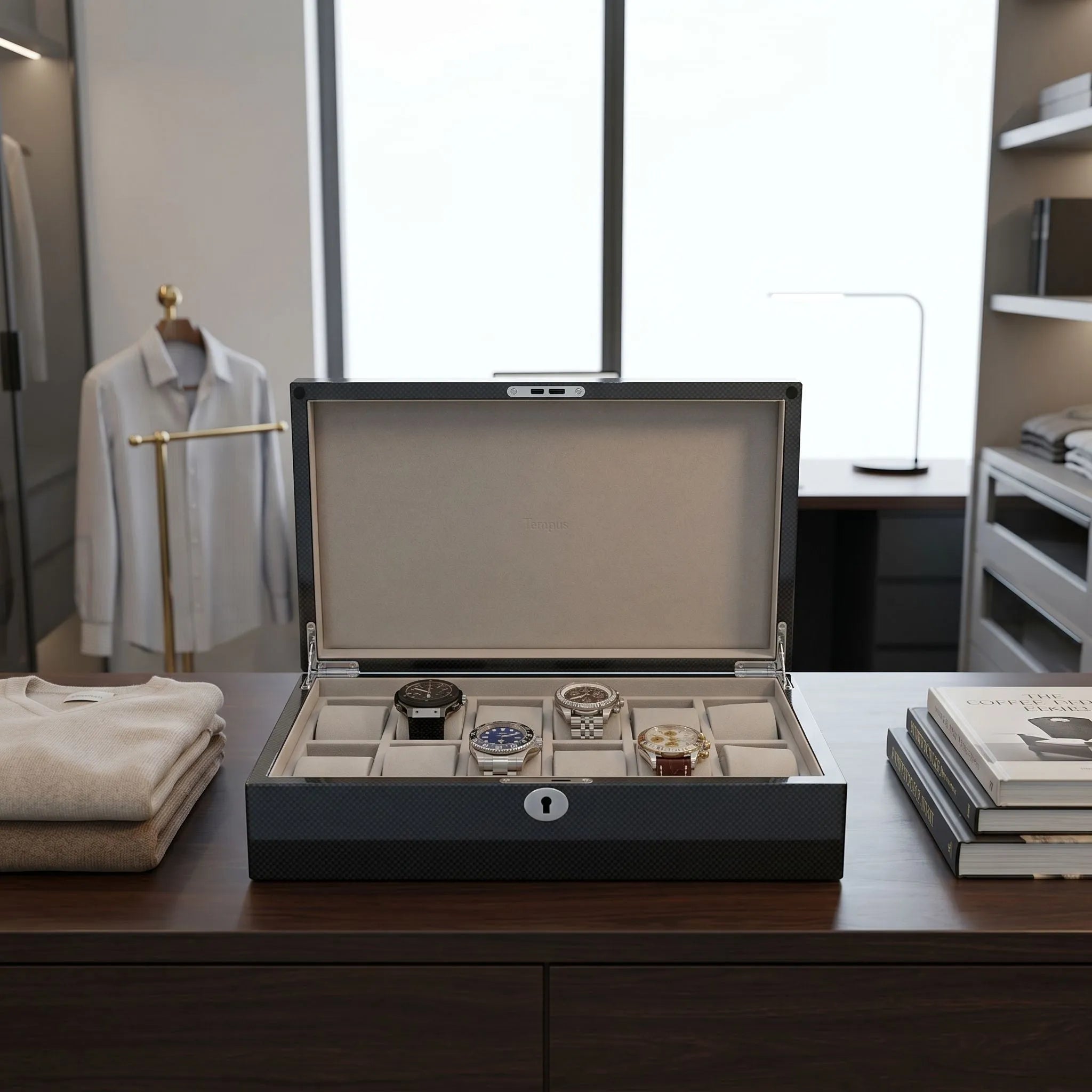 Front view of 12-watch box with curved lid in modern dressing room, highlighting its size, carbon fibre finish, and secure watch compartments.