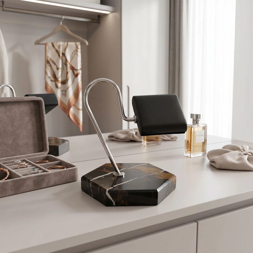 Full-height view of Tempus watch stand on dressing room vanity with jewelry props, highlighting hexagon marble base and black leather cushion in a bright modern setting.