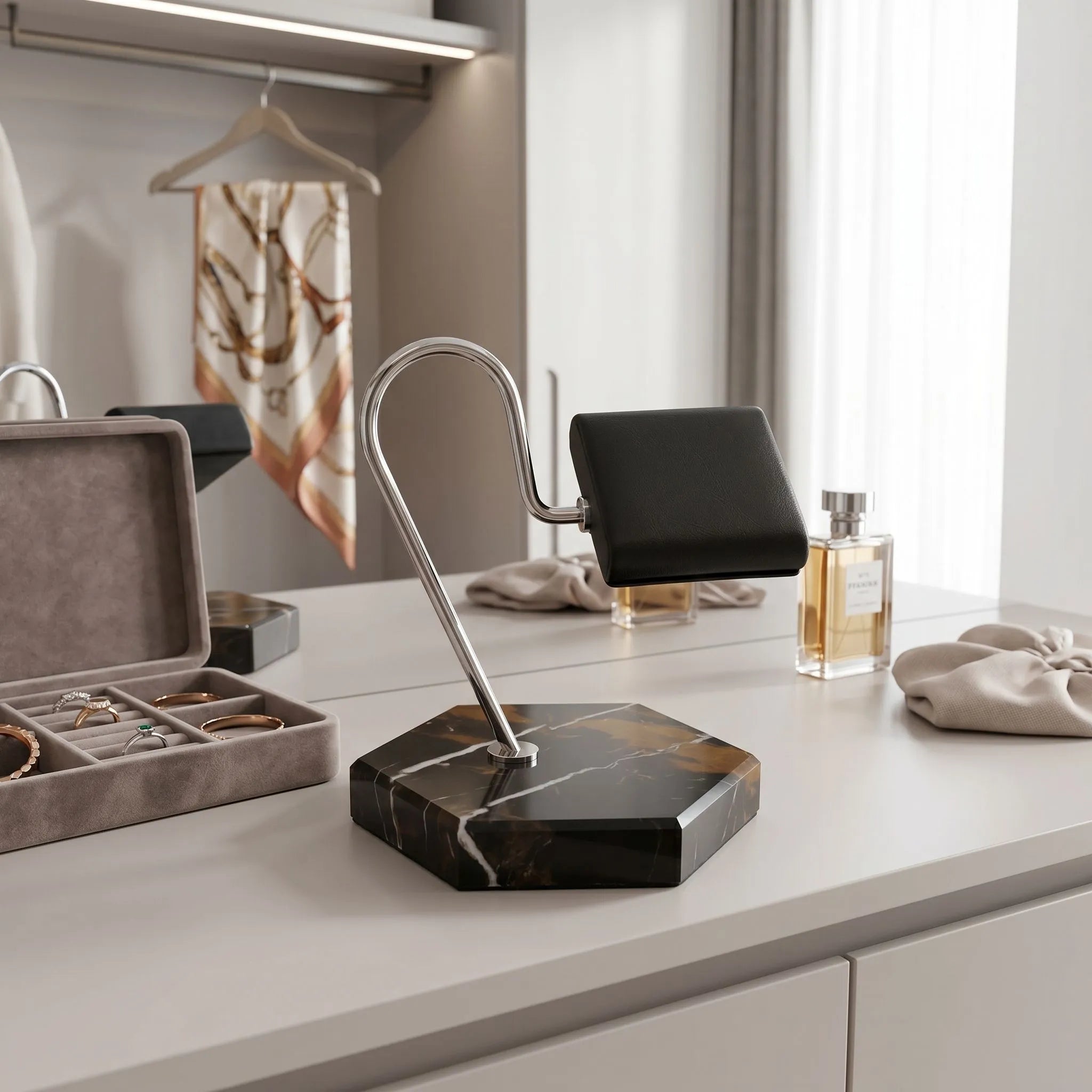 Full-height view of Tempus watch stand on dressing room vanity with jewelry props, highlighting hexagon marble base and black leather cushion in a bright modern setting.