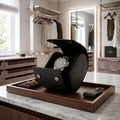Close-up of black saffiano leather watch roll with dark metal closures and soft black lining, in a bright modern dressing room.