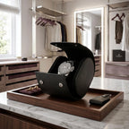 Close-up of black saffiano leather watch roll with dark metal closures and soft black lining, in a bright modern dressing room.